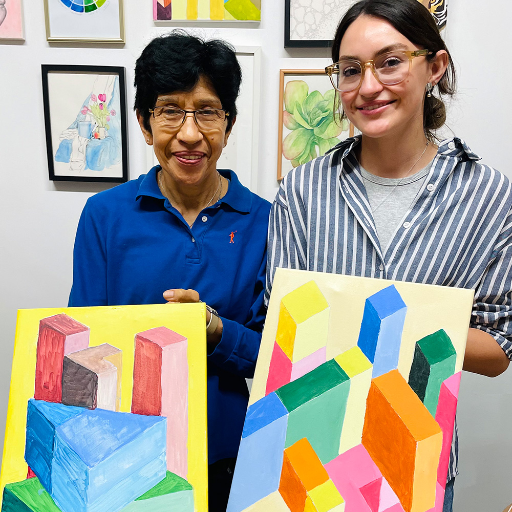 2 women smiling holding paintings